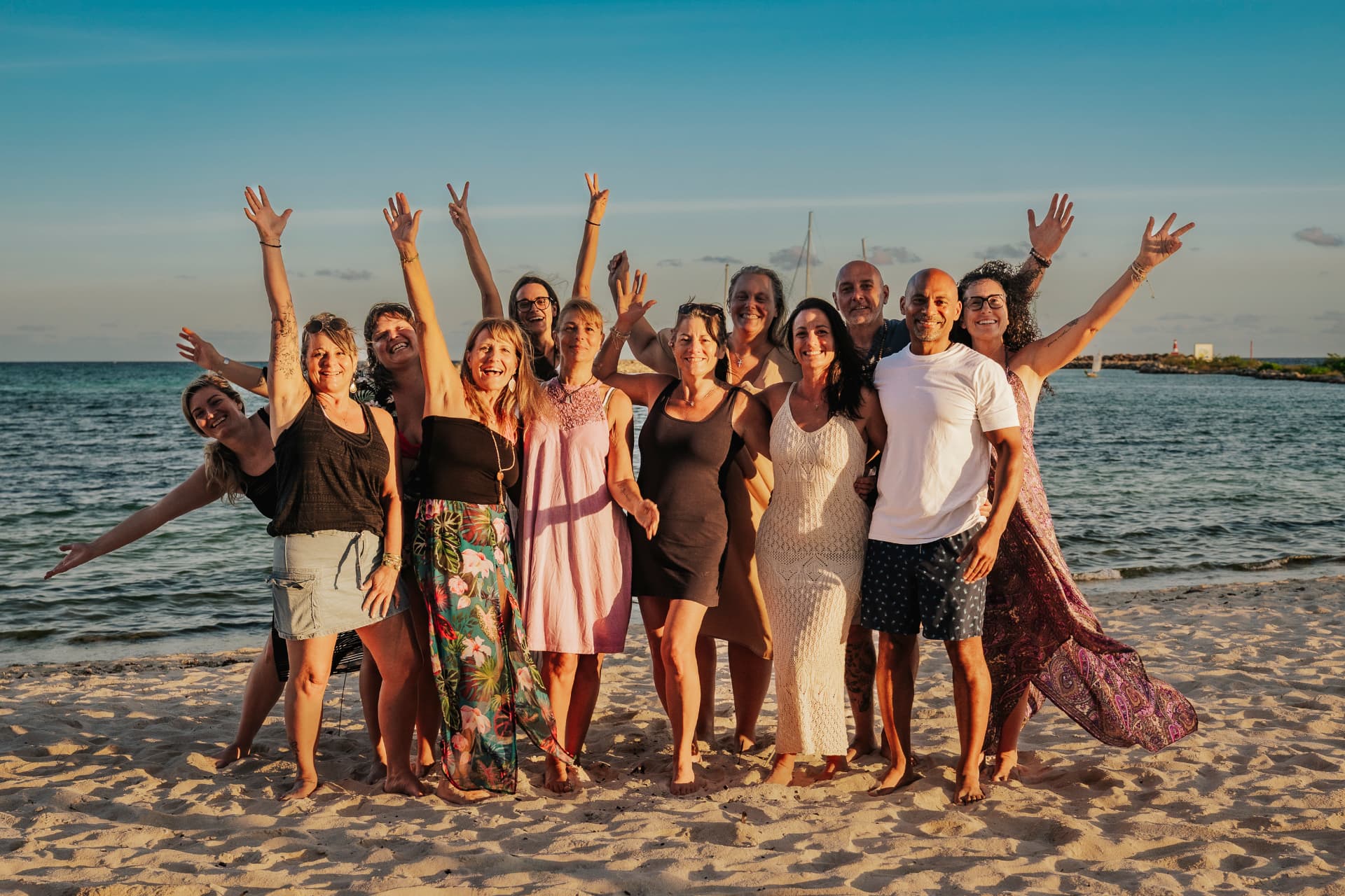 Groupe joyeux les bras en l'air sur la plage au coucher du soleil