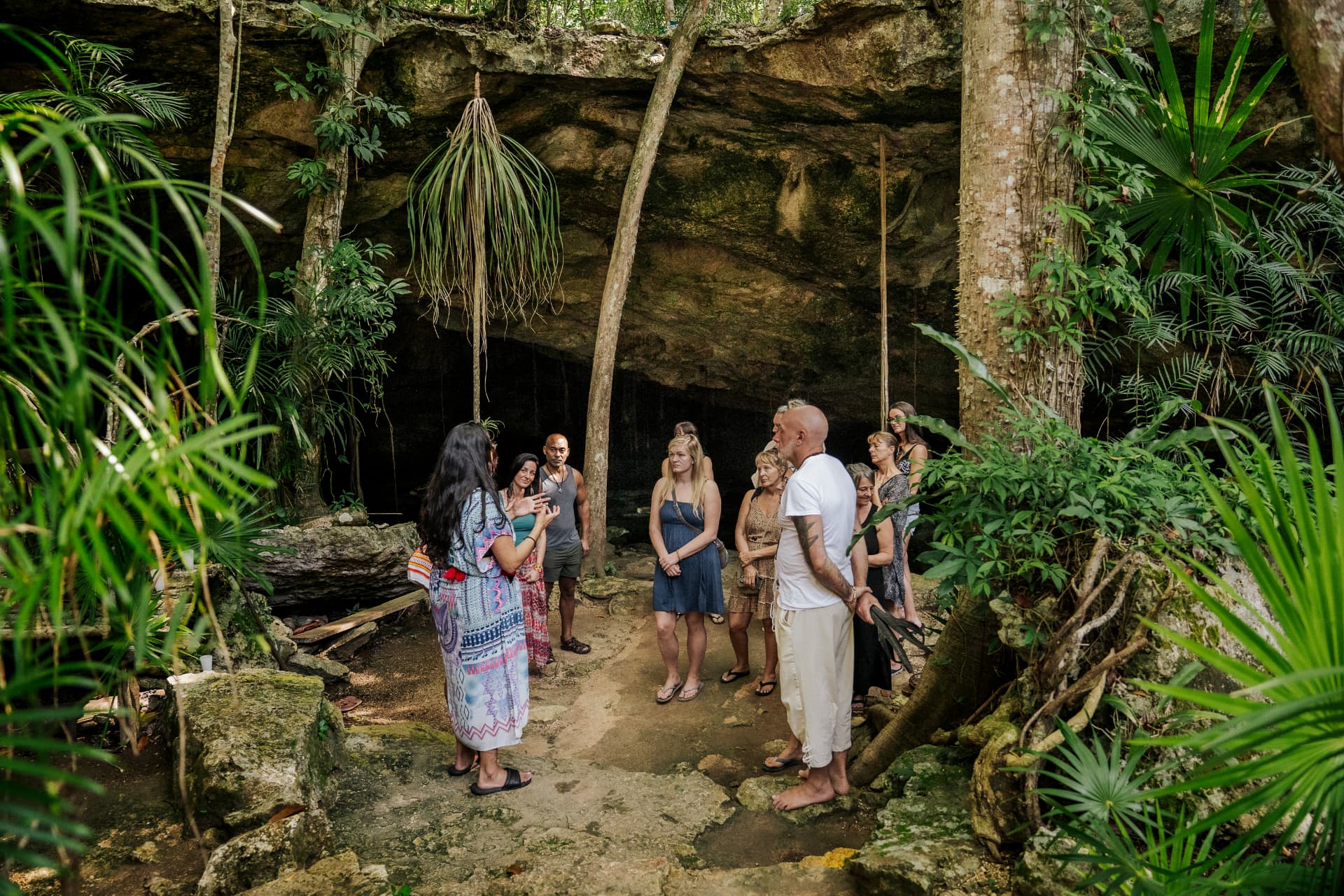 Groupe de voyageurs écoutant une guide devant l'entrée d'un cénoté