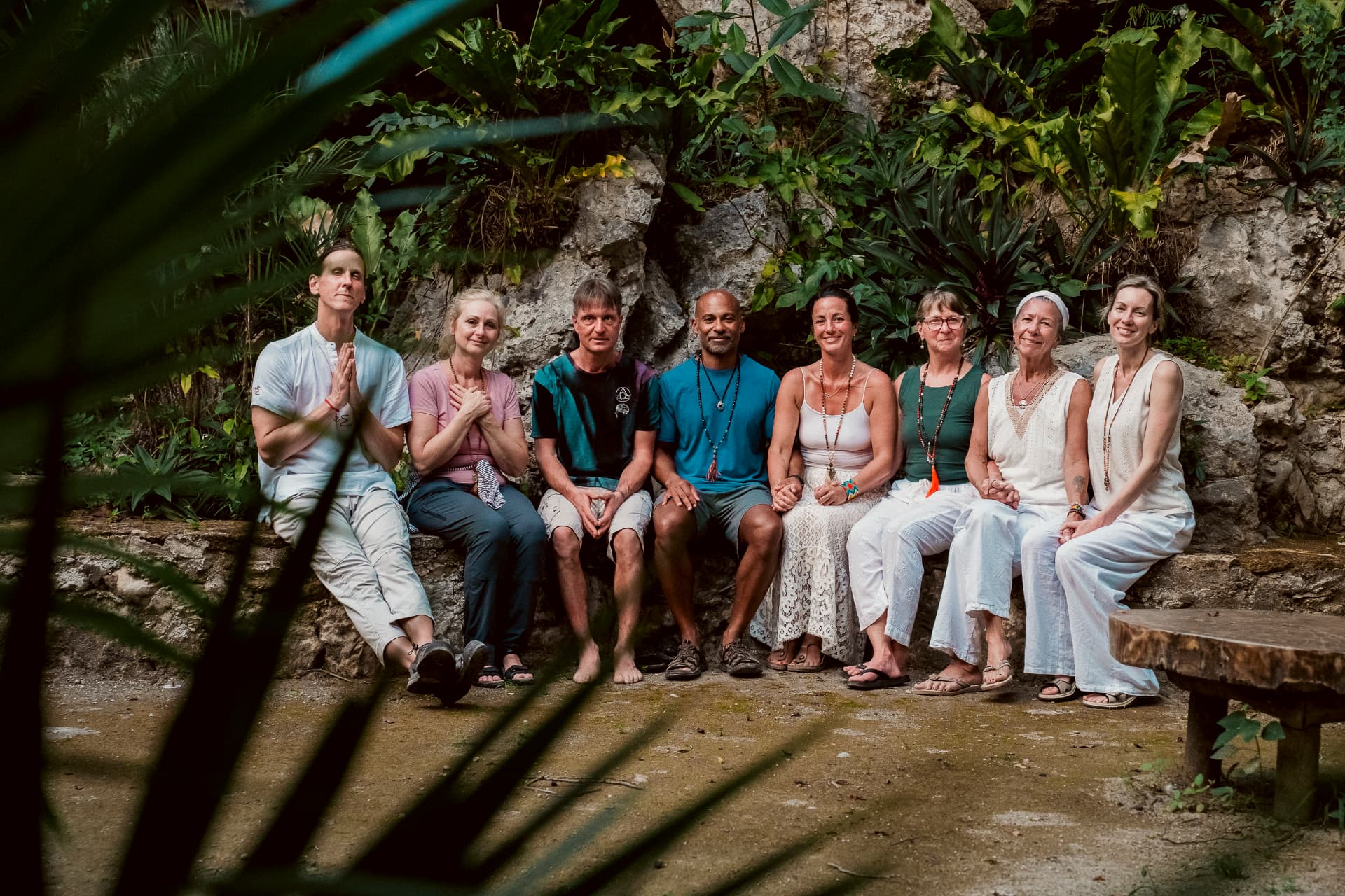 Groupe assis en méditation devant un mur de pierre couvert de plantes tropicales